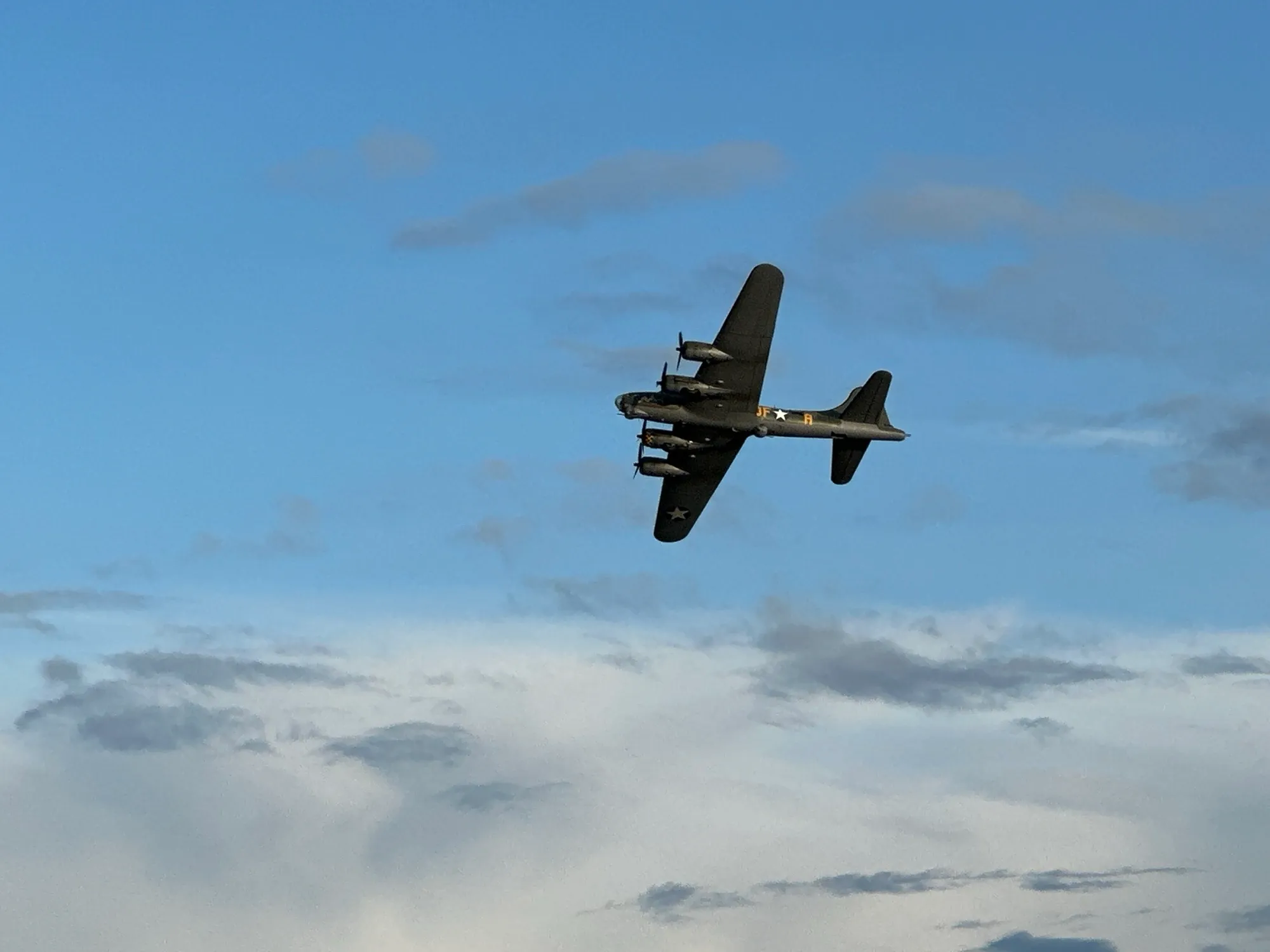 A B-17 Flying Fortress banking overhead against blue sky and broken cloud