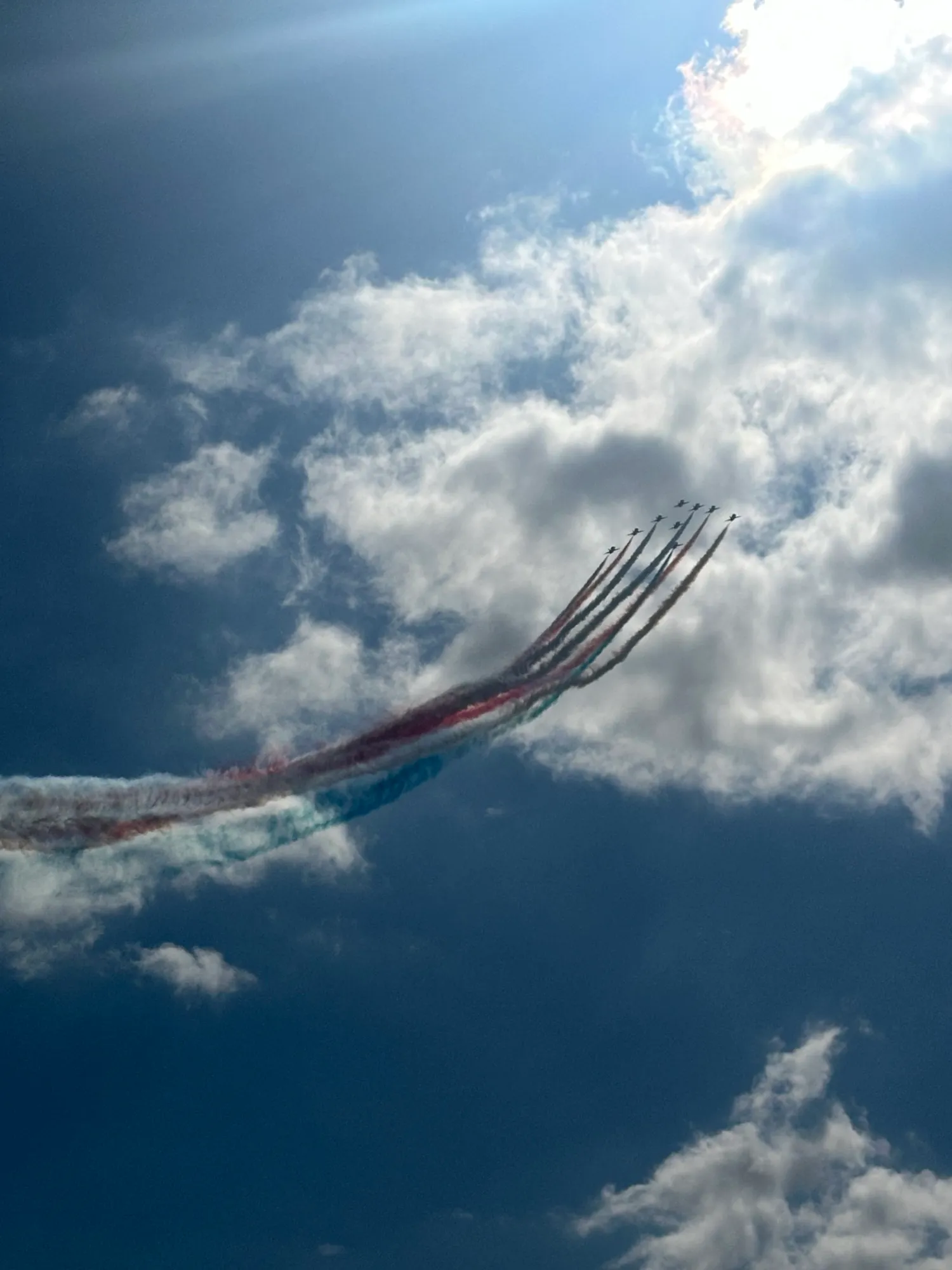 Red Arrows in tight formation leaving a red, white and blue smoke trail through backlit cloud