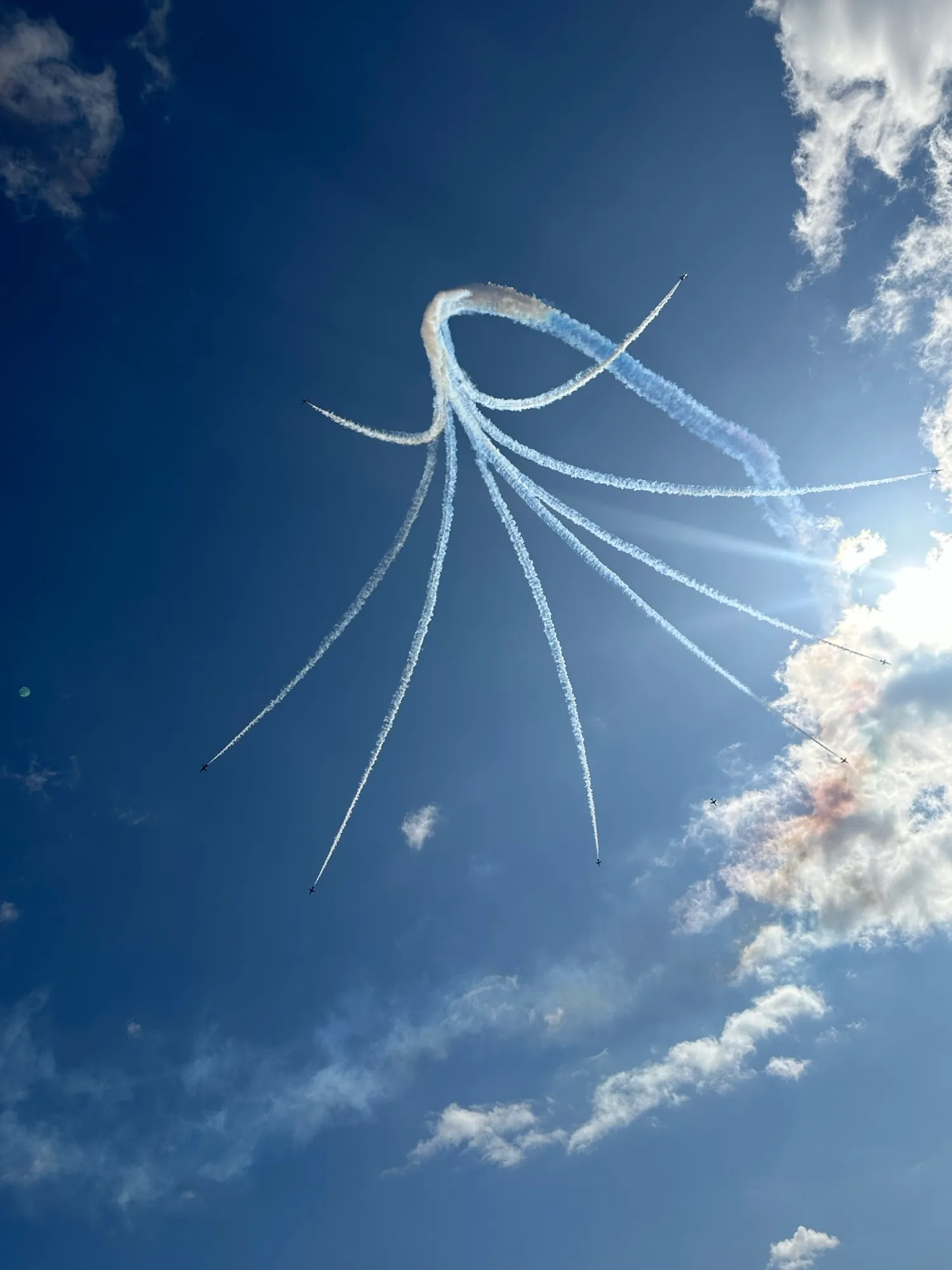 Red Arrows trailing smoke in a looping pattern against a deep blue sky with the sun low on the right